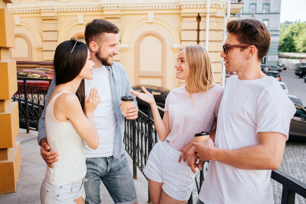 Two young couples talking to each other outside.