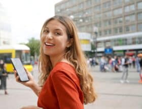 Smiling woman holding phone on the street.