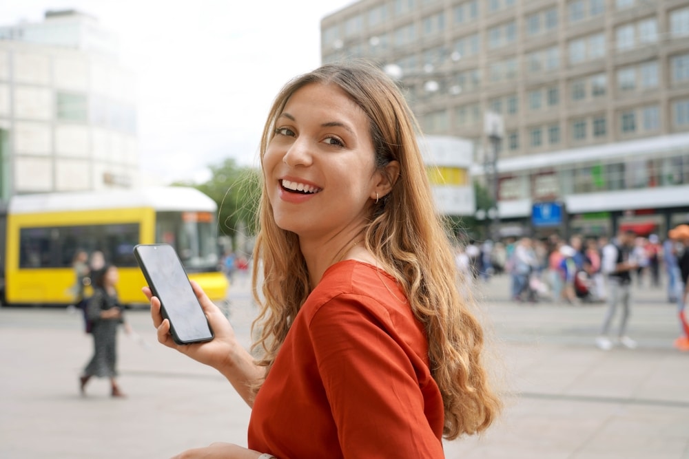 Smiling woman holding phone on the street.